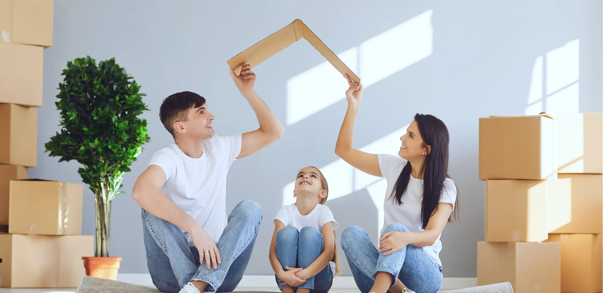 Família montando o telhado de uma casa com papelão em meio às caixas da mudança